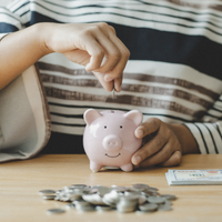 Person putting coins and paper money into a piggy bank